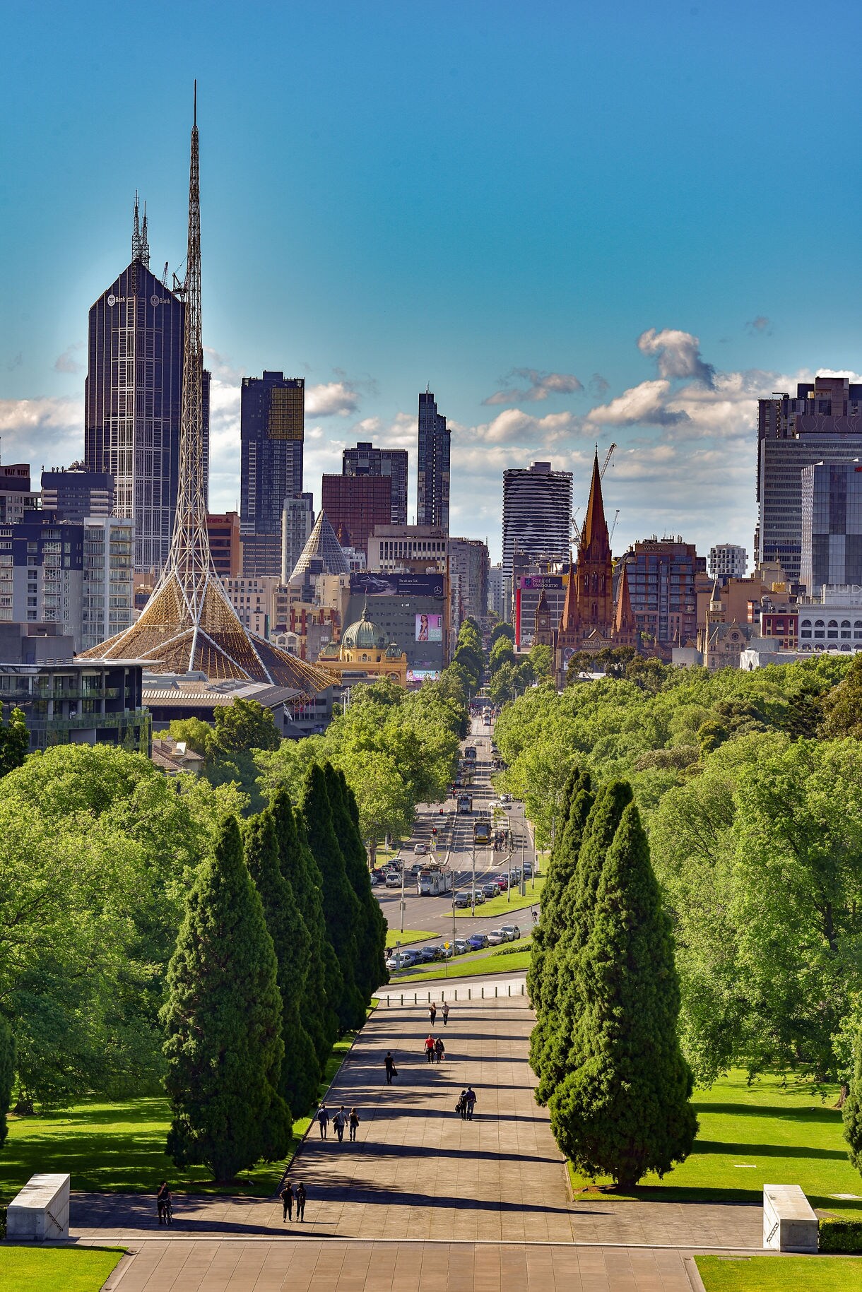 iew from the Shrine of Remembrance in Melbourne showing a tree-lined avenue leading toward the city center with skyscrapers, historic buildings and trams.