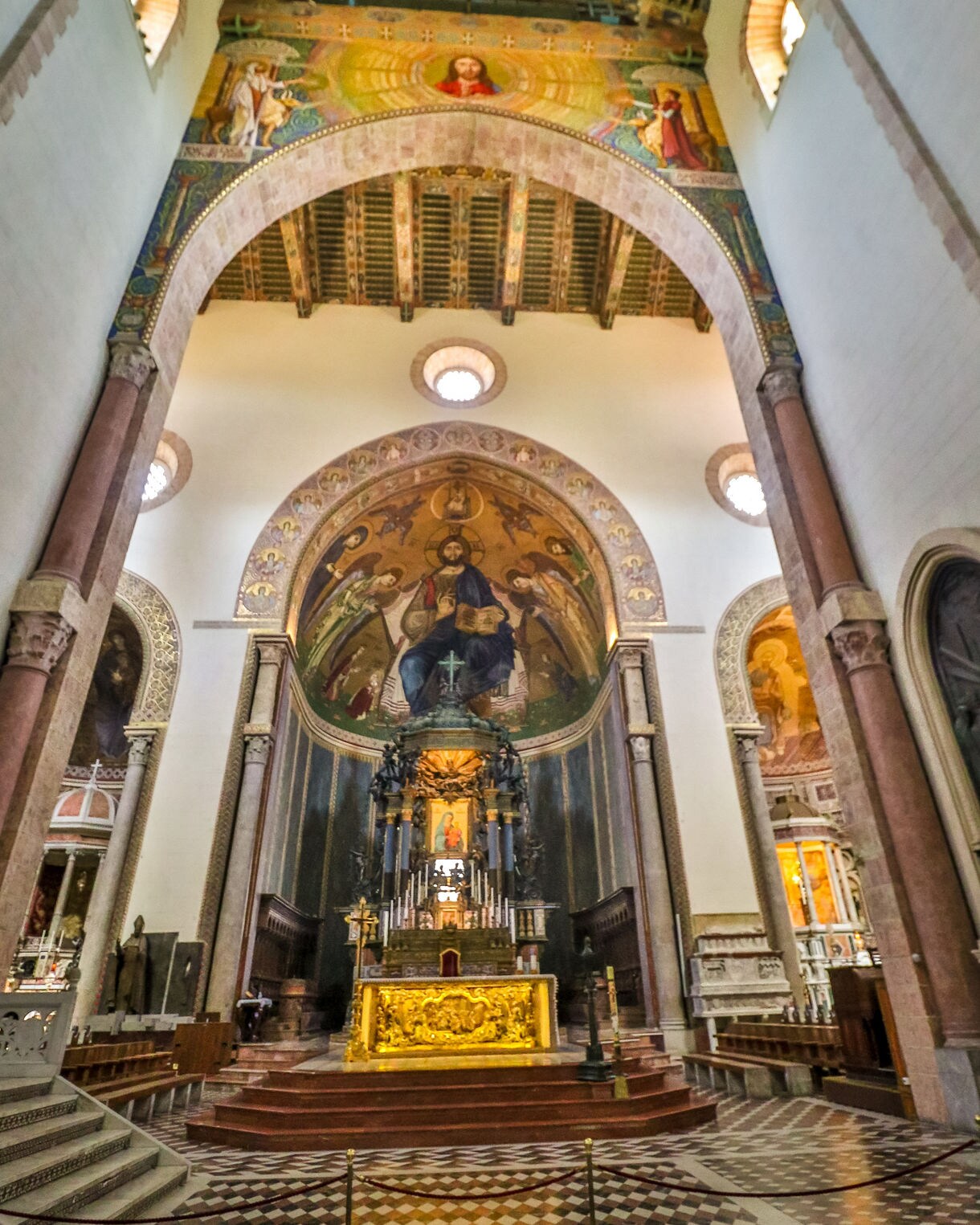 Interior of a grand Sicilian cathedral featuring an ornate golden altar, large religious frescoes, marble columns and a richly decorated wooden ceiling.