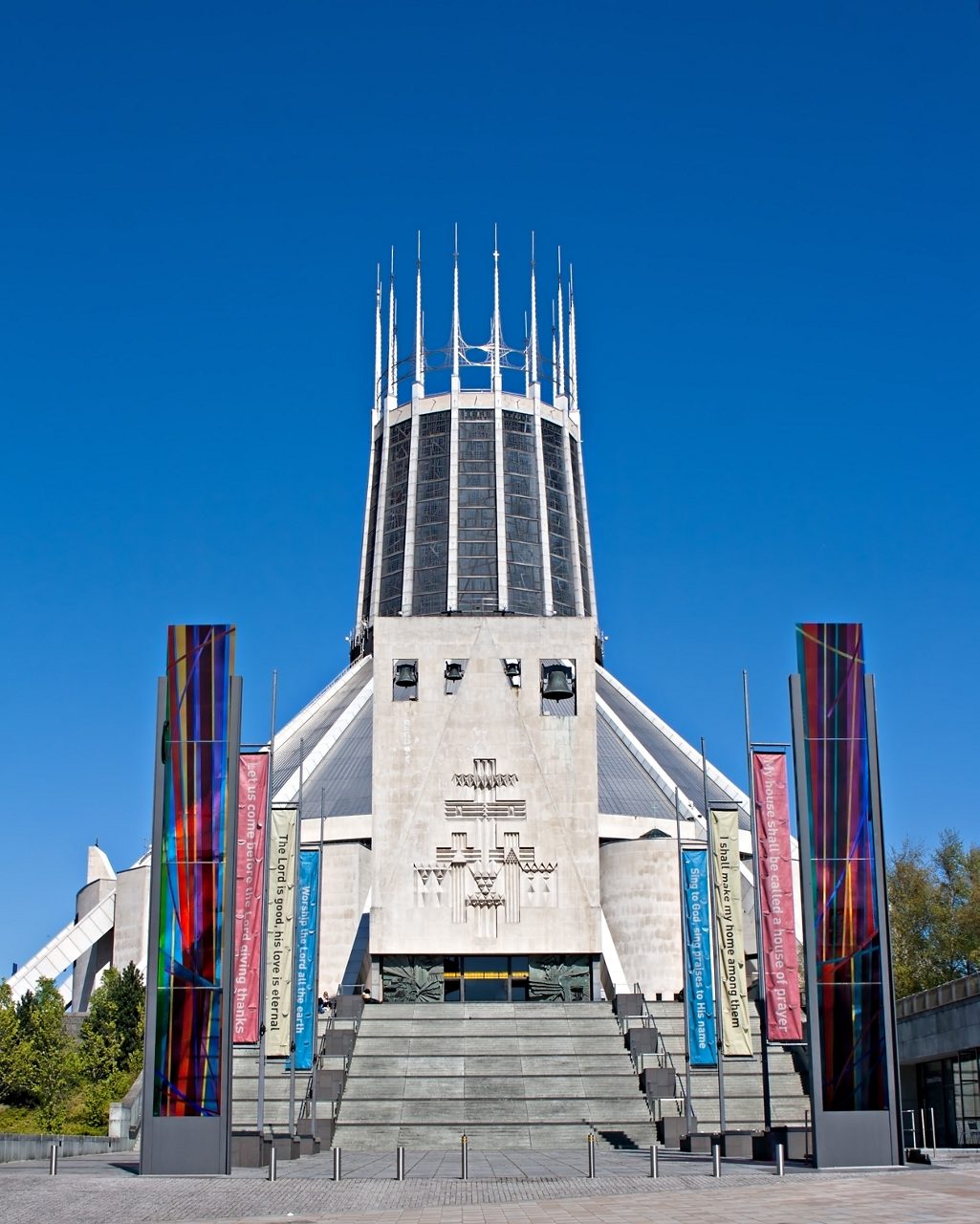 Front view of the Metropolitan Cathedral in Liverpool, featuring its circular structure, tall spires and colorful glass pillars against a clear blue sky.