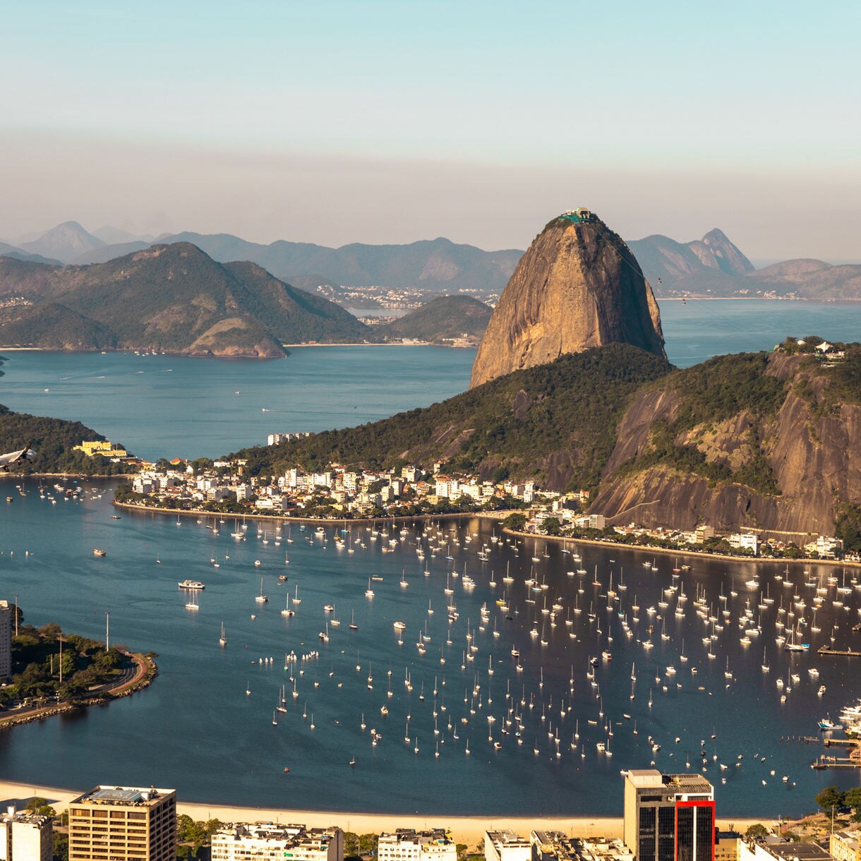 Aerial view of Rio de Janeiro from Mirante Dona Marta, showing Sugarloaf Mountain, Guanabara Bay filled with boats and the city’s coastline backed by distant green mountains.