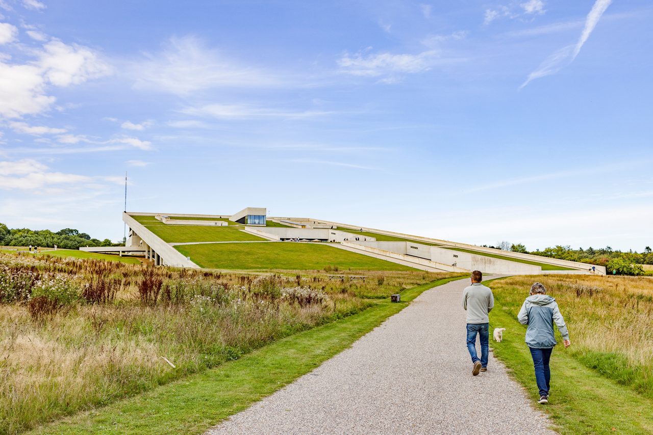 Moesgaard Museum in Denmark with sloping green roof blending into grassy landscape under blue sky.