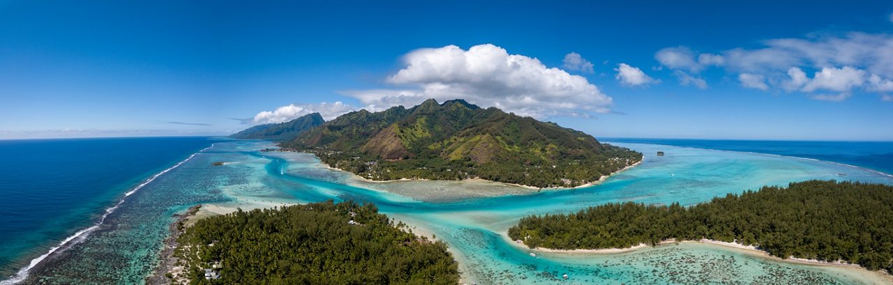 Aerial view of Moorea, French Polynesia, with lush green mountains, coral reefs and bright turquoise lagoons merging into the deep blue Pacific.