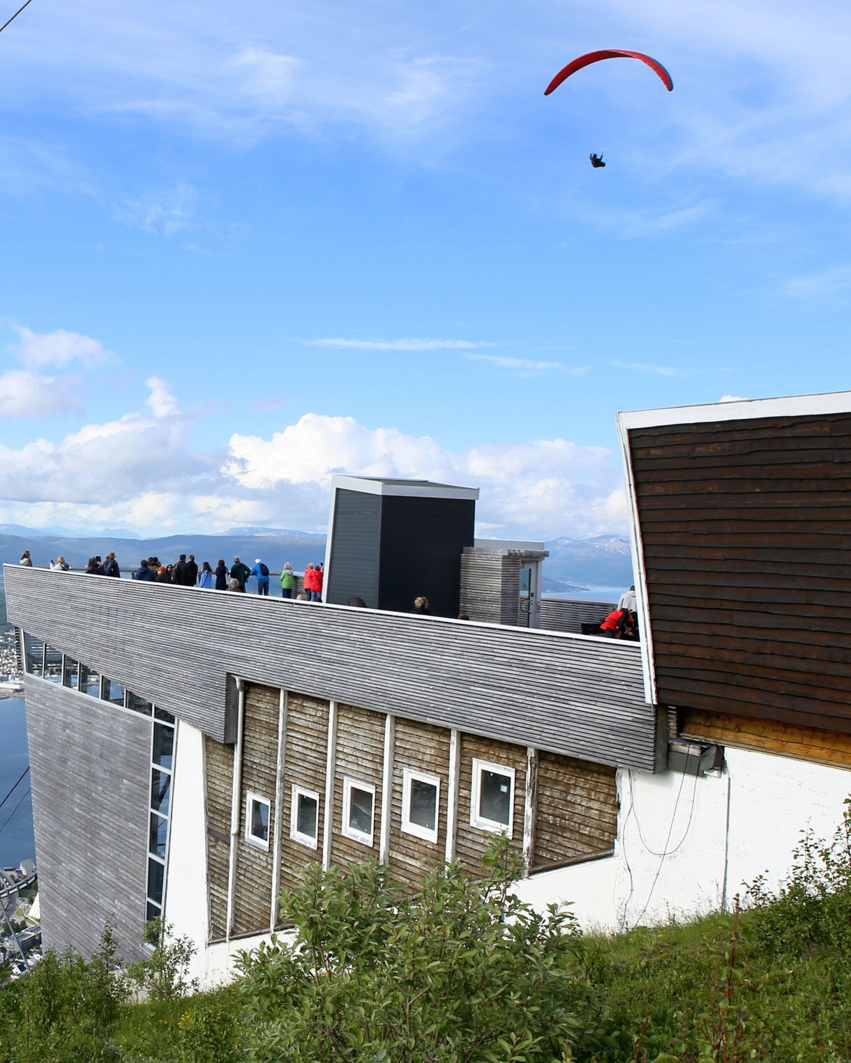 Observation deck on Mt. Storsteinen overlooking Tromsø’s harbor, bridge and mountains, with a paraglider in the sky.