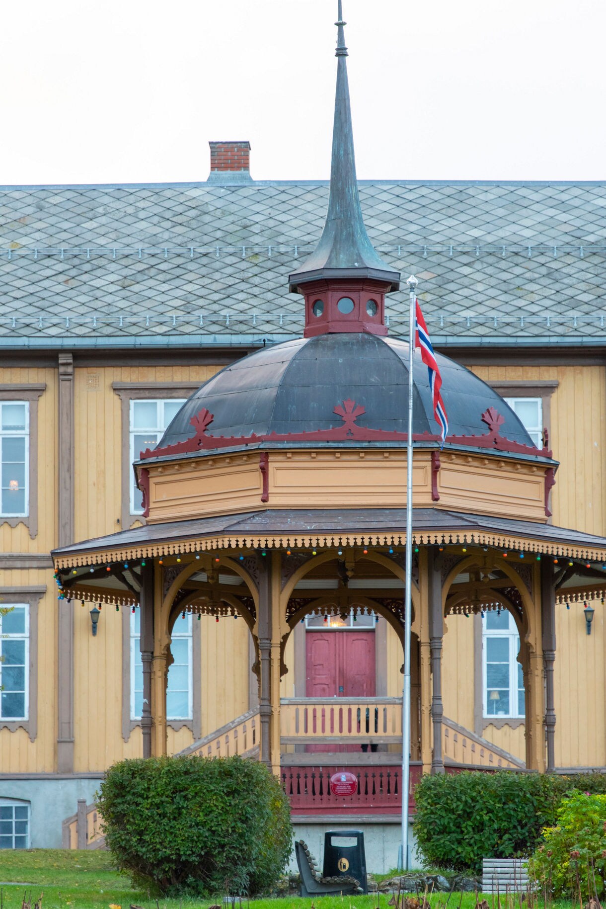 Close-up of a wooden music pavilion with a spire and Norwegian flag in Tromsø.