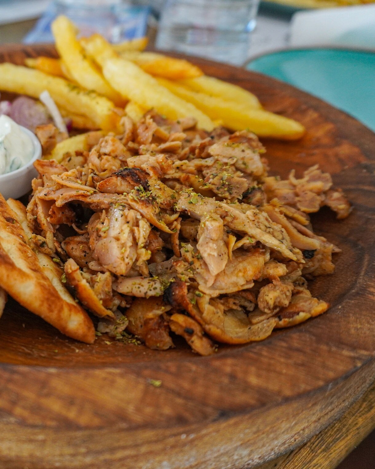 Greek gyro platter on a wooden board with sliced pita, grilled meat, fries, tomato, onion and tzatziki sauce.