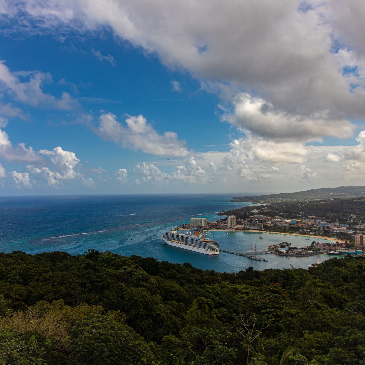 A panoramic view from Mystic Mountain in Jamaica overlooking Ocho Rios, a cruise ship docked in the harbor and the Caribbean Sea stretching into the horizon.