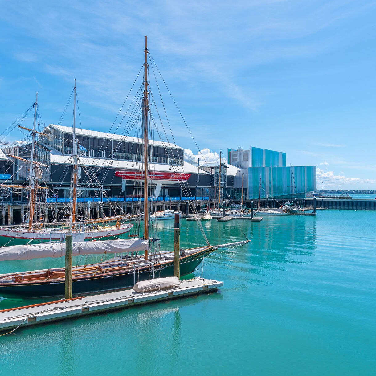 Boats and yachts docked outside the National Maritime Museum in Auckland, New Zealand, with turquoise harbor waters and modern waterfront buildings.
