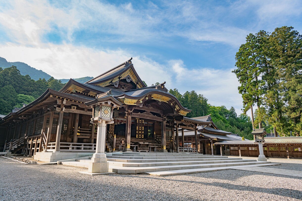  A wide-angle view of Yahiko Shrine in Niigata, Japan, featuring ornate wooden buildings with curved roofs trimmed in gold, set against tall evergreens and a clear blue sky.