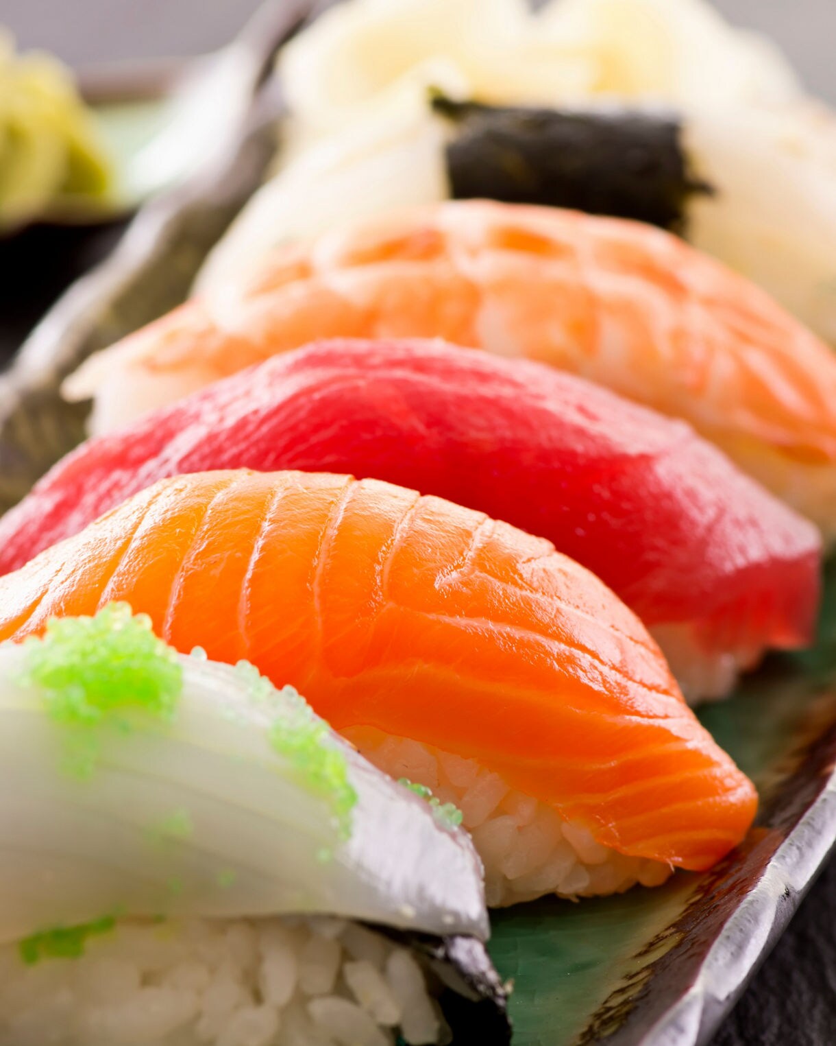 Close-up of assorted nigiri sushi arranged on a ceramic plate, featuring pieces of salmon, tuna, squid and shrimp with bright colors and glossy textures.
