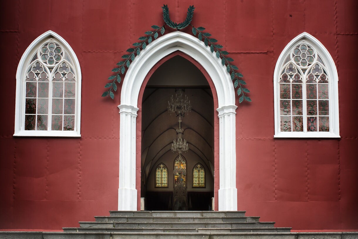 Gothic-style entrance of the red iron church with white arched doorway and stained glass windows in Grecia, Costa Rica.