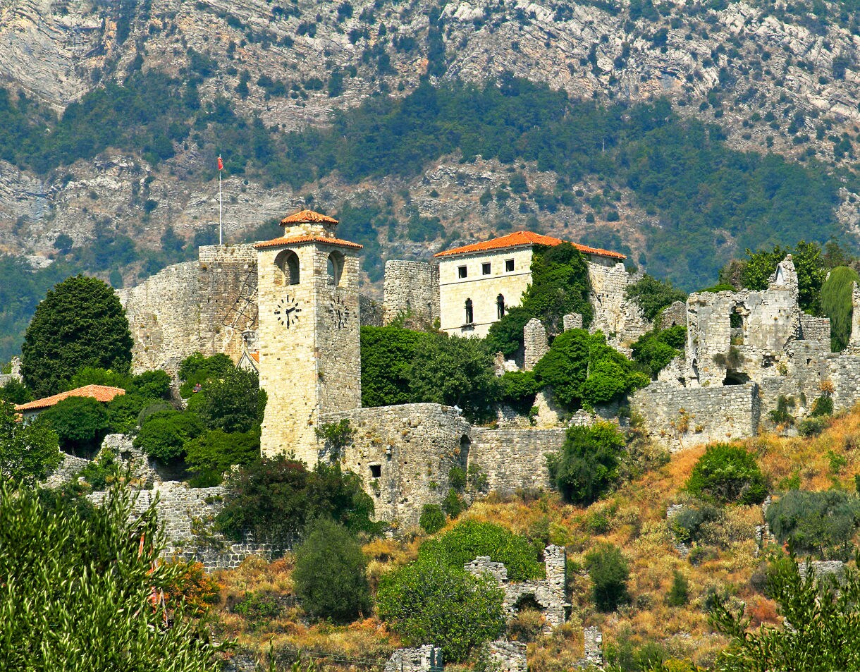 Ruins of Old Bar fortress set against steep green mountains with crumbling stone towers and walls.