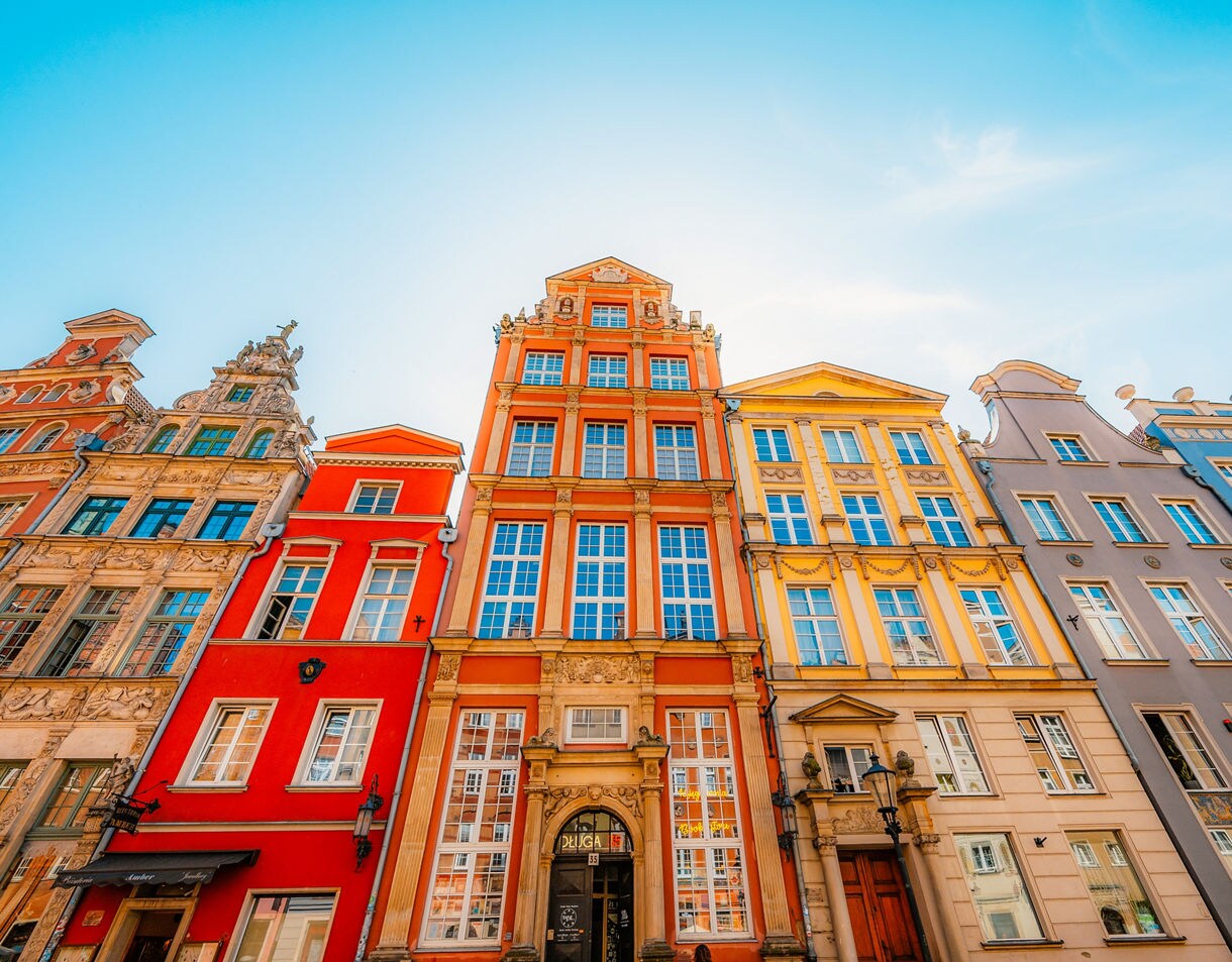 Row of vibrant historic buildings in Gdańsk’s Old Town, painted in red, yellow, blue and pastel shades with ornate details.