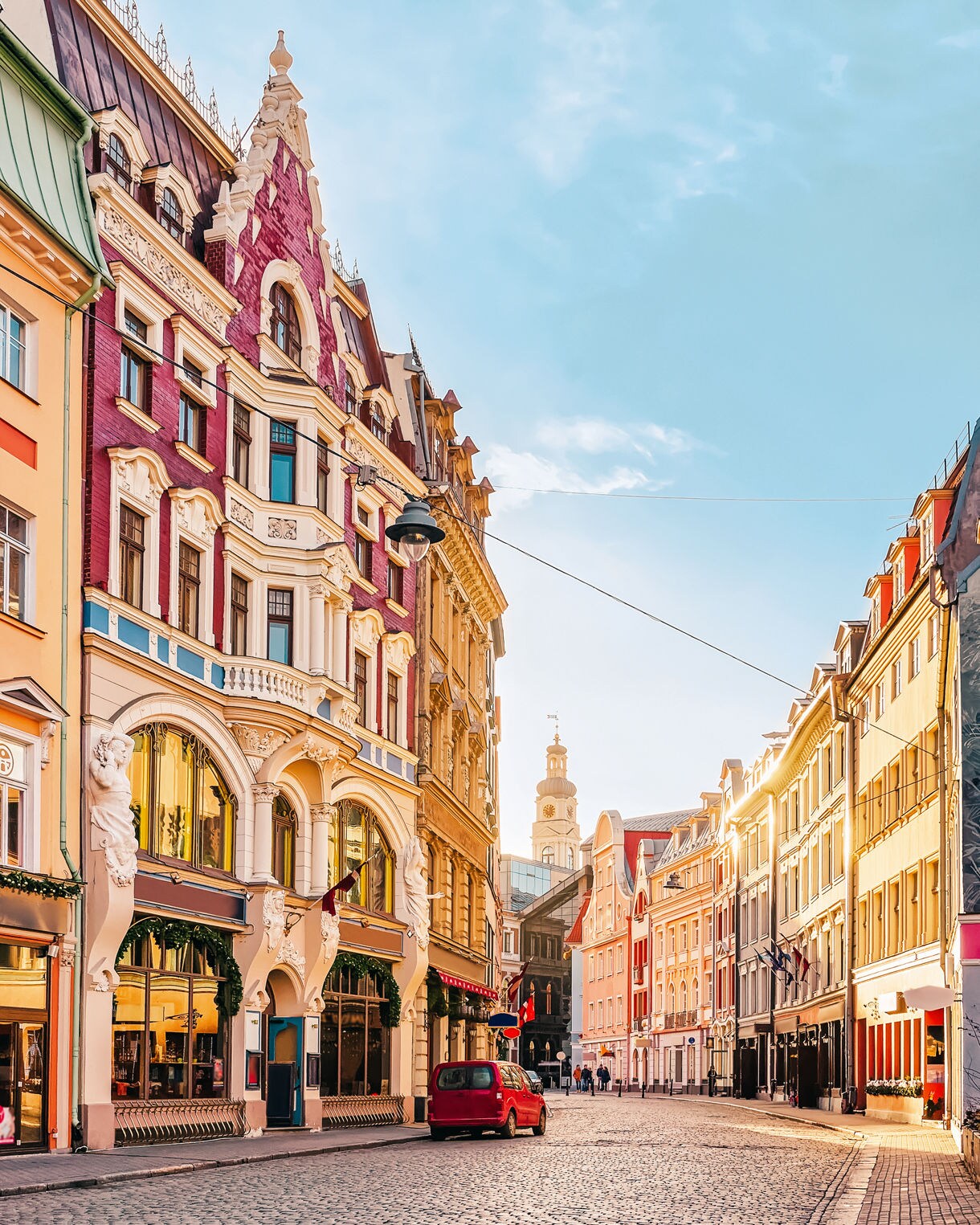 Street view of Old Town Riga, Latvia, with ornate pastel buildings, cobblestone pavement and warm sunlight reflecting off historic architecture.