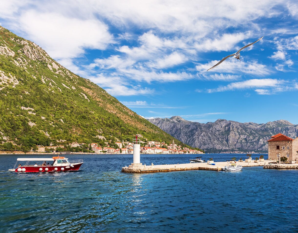 Stone church with a red-tiled roof on Our Lady of the Rocks, a small man-made island in the Bay of Kotor, Montenegro, surrounded by blue waters and mountains.