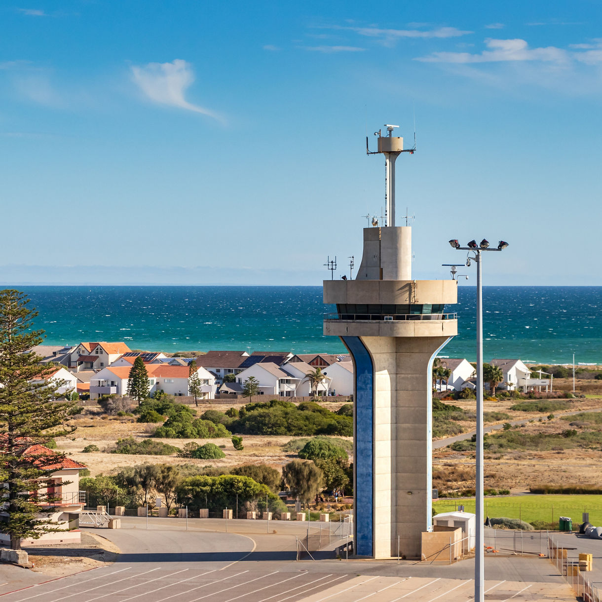 A tall control tower at Adelaide’s Outer Harbor with coastal houses, greenery and the ocean in the background.