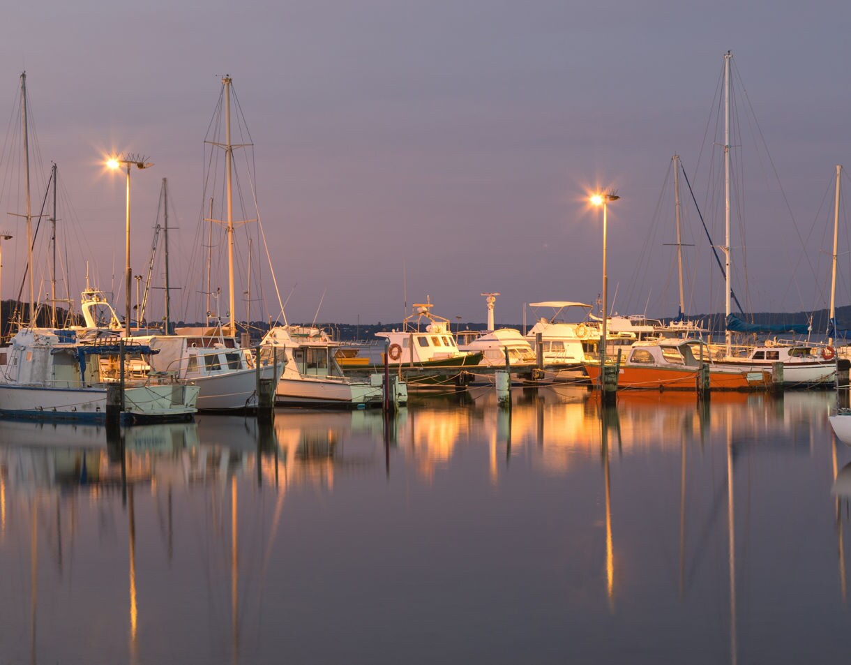 Docked boats reflecting warm lights on still water at dusk.