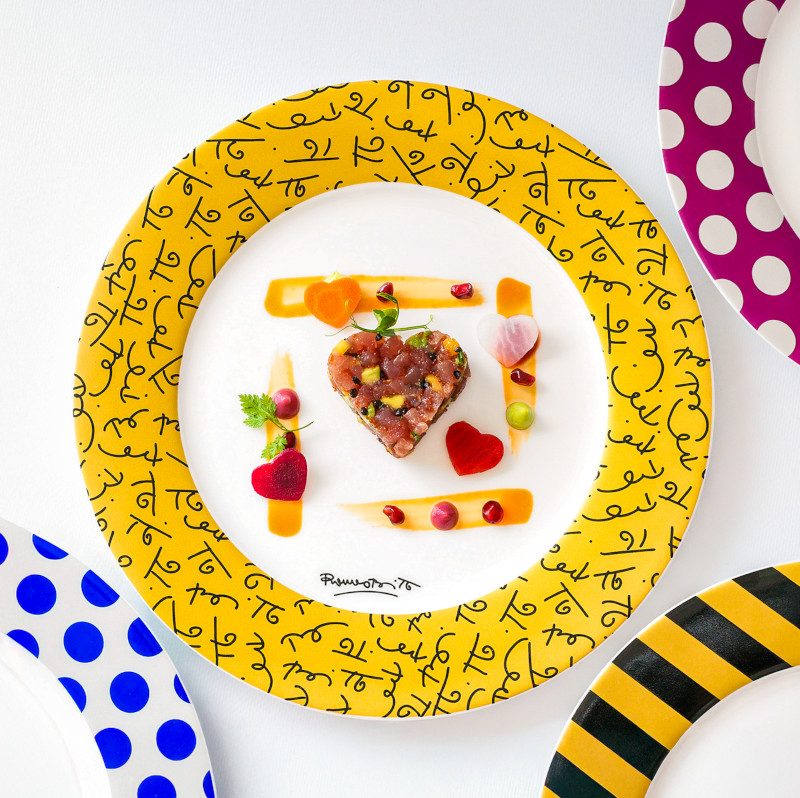 A plated dessert with a heart motif surrounded by a gold-patterned rim and colorful polka dot accents. 