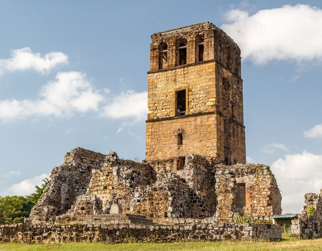 Ancient stone tower and surrounding ruins of Panamá Viejo standing under a bright sky with scattered clouds.