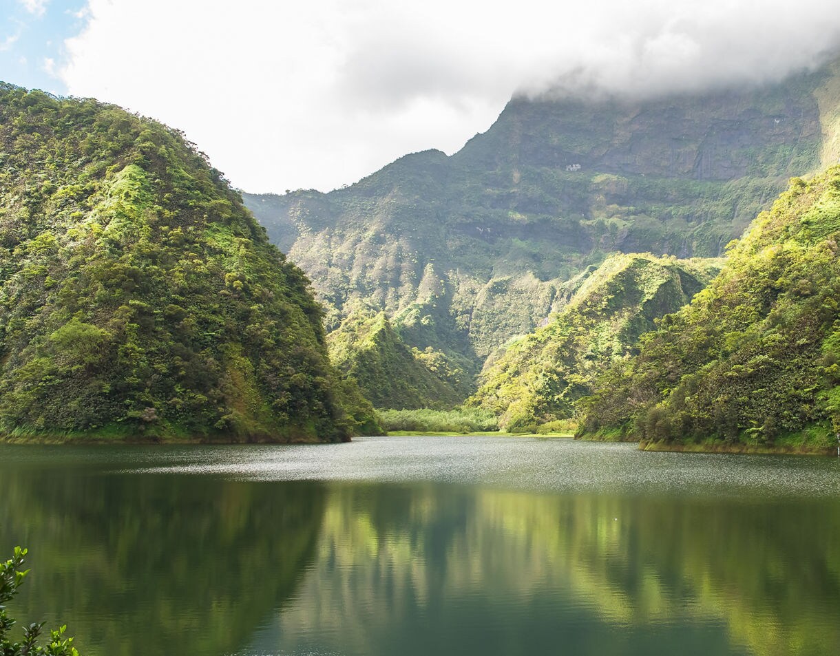 Quiet lake surrounded by steep green mountains in Tahiti’s Papenoo Valley with clouds hanging over the tallest peaks.