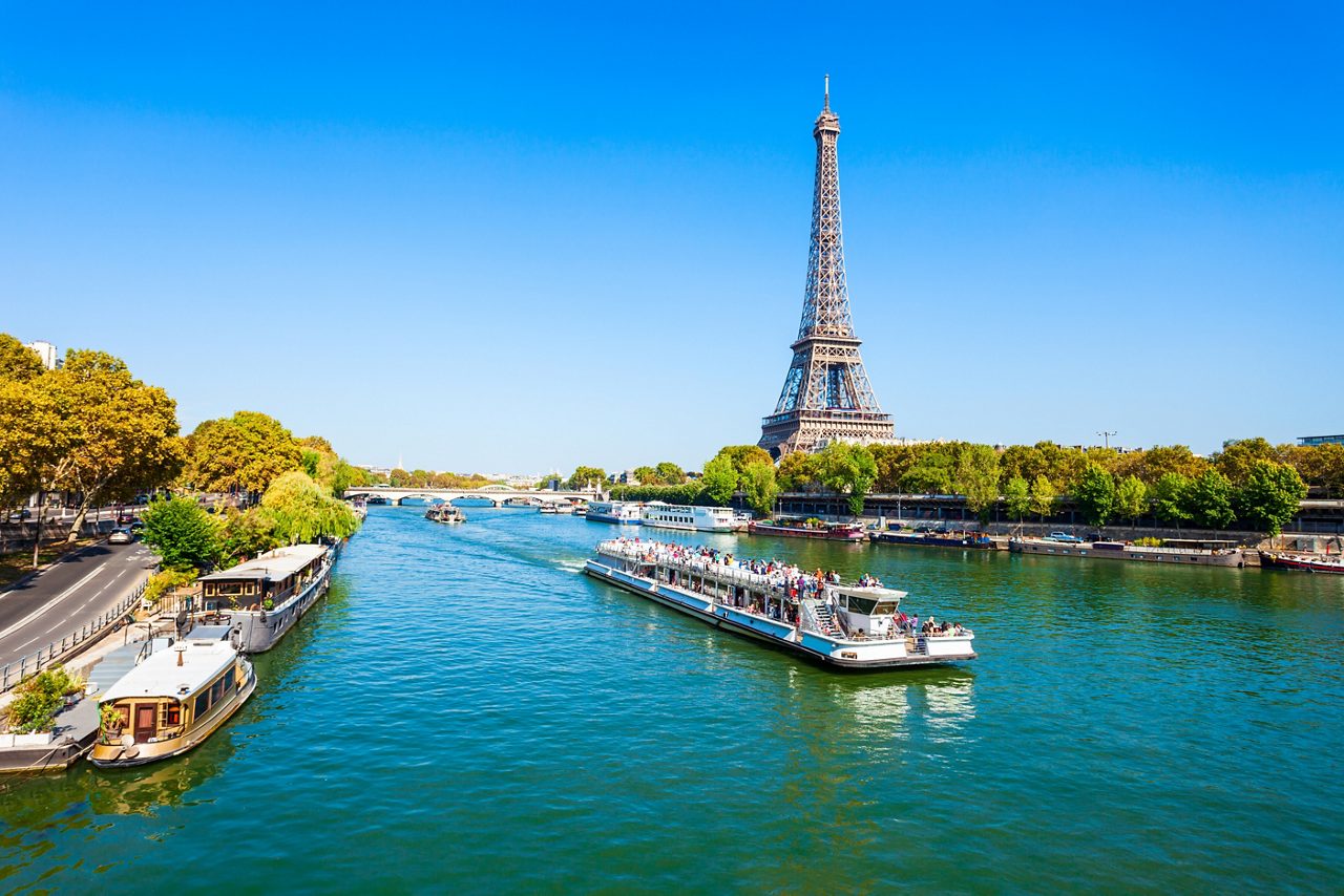 Panoramic view of Paris at dusk with the Eiffel Tower towering over rooftops and tree-lined boulevards under a pastel sky.