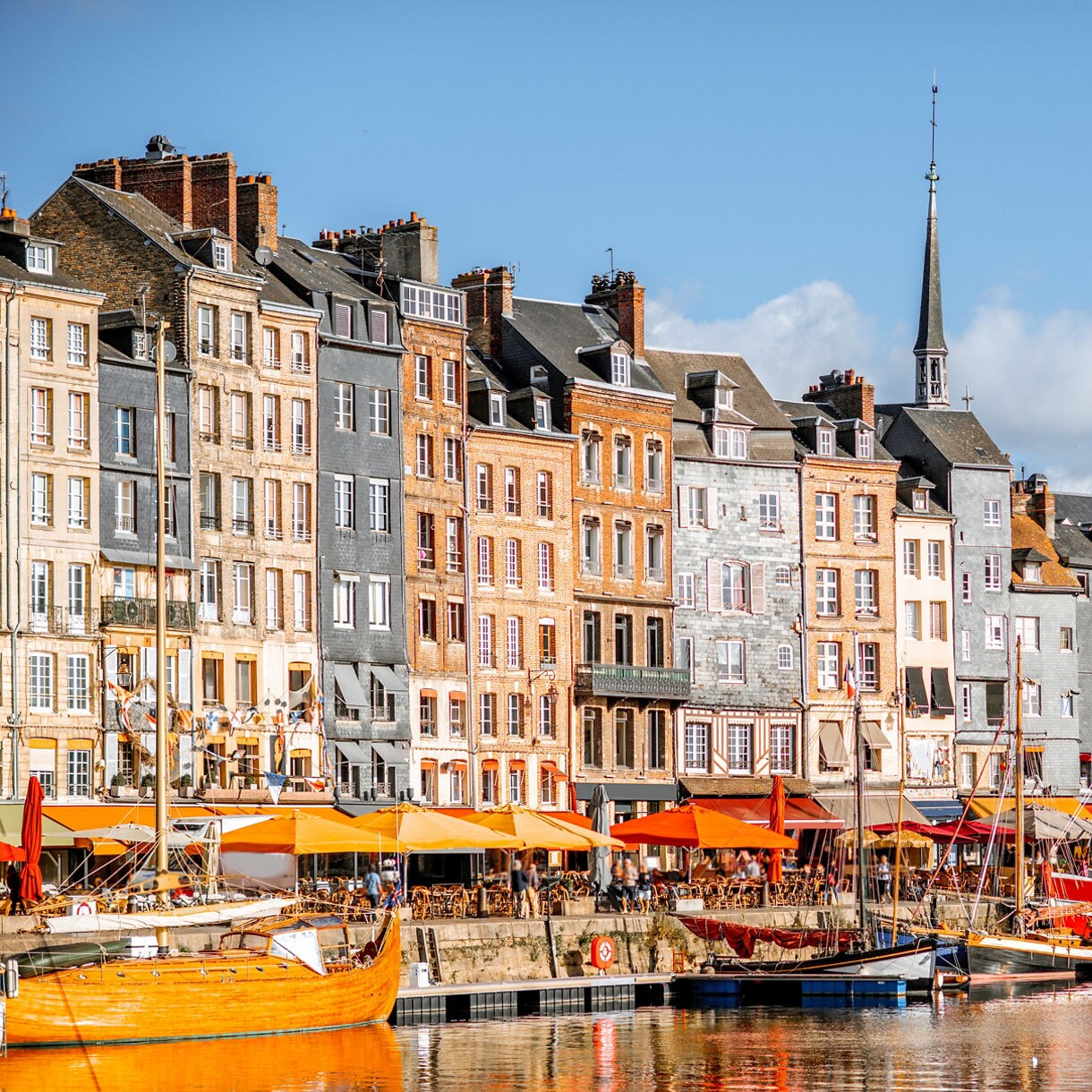 Row of tall, colorful buildings with boats docked along the harbor in Honfleur, France.