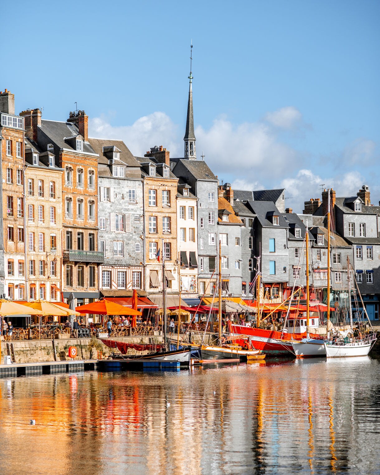 Colorful waterfront buildings with sailboats and café terraces reflecting in the harbor at Honfleur.