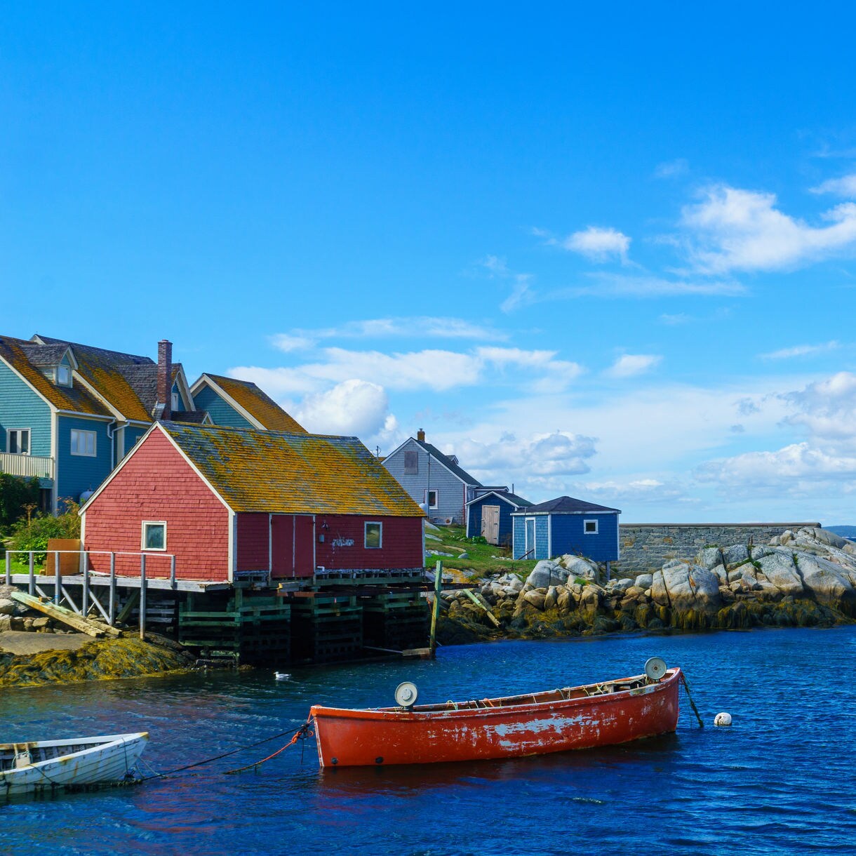 Coastal scene at Peggy’s Cove with brightly painted houses, a rocky shoreline and an old red boat floating on deep blue water.
