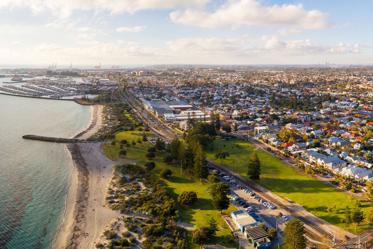 Aerial view of Fremantle coastline with sandy beaches, marina, green parks and sprawling suburbs under soft afternoon light.