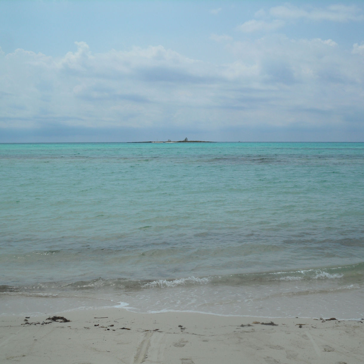 View of Peterson Cay National Park, showing turquoise ocean waters, a sandy shoreline and a small island in the distance under cloudy skies.