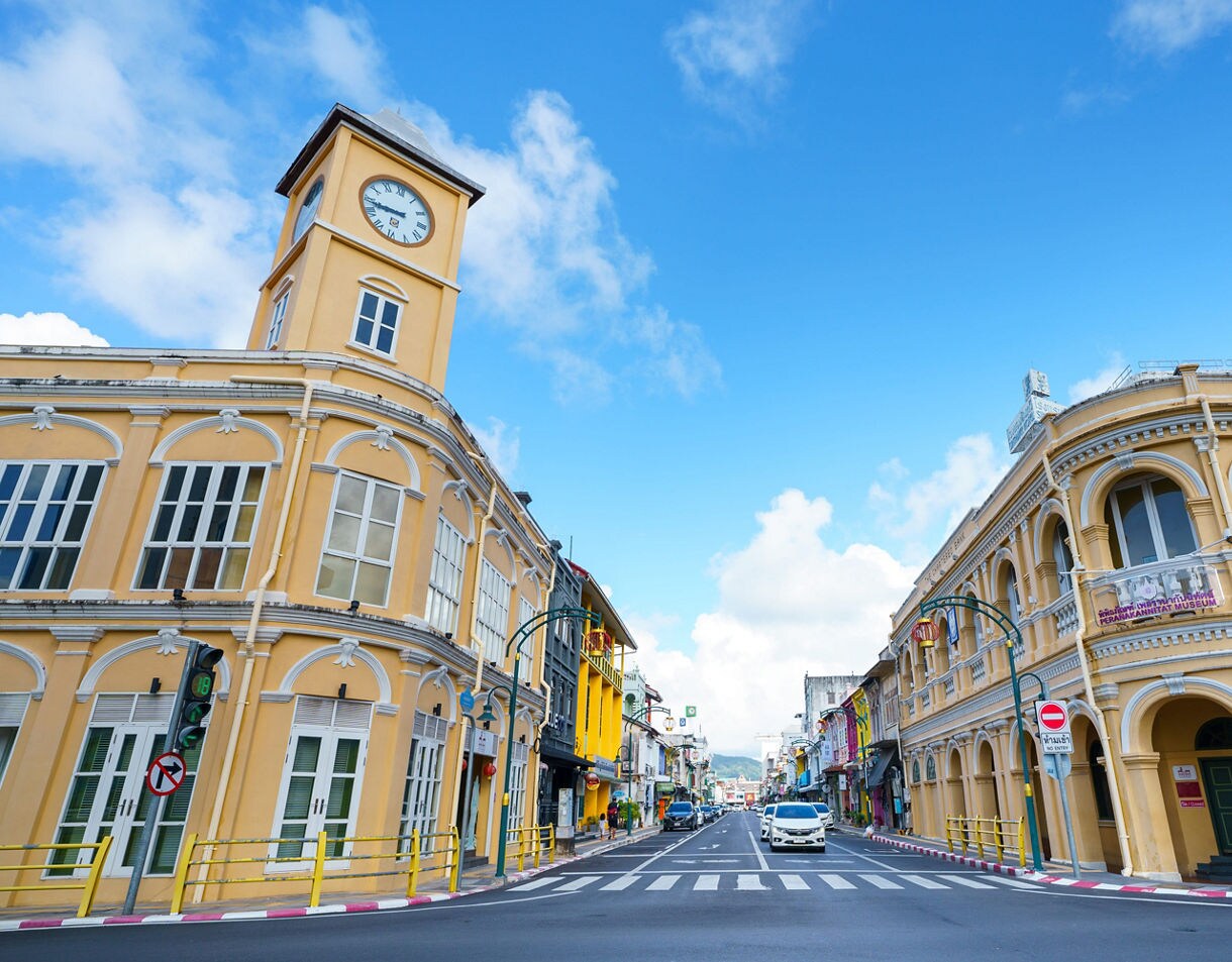 Street view of Phuket Old Town featuring yellow Sino-Portuguese buildings with arched windows and a clock tower.