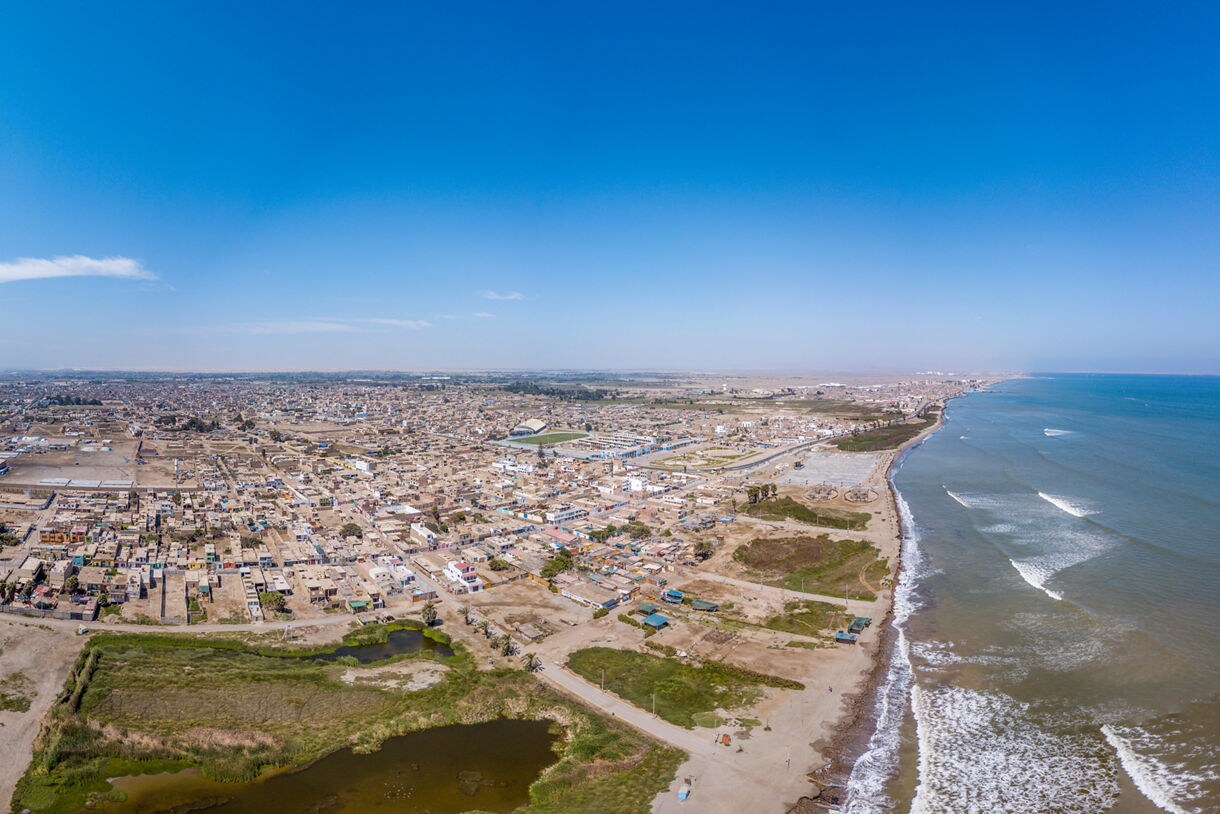 Aerial view of Pisco, Peru showing a sprawling desert city beside a long Pacific shoreline with gentle waves.