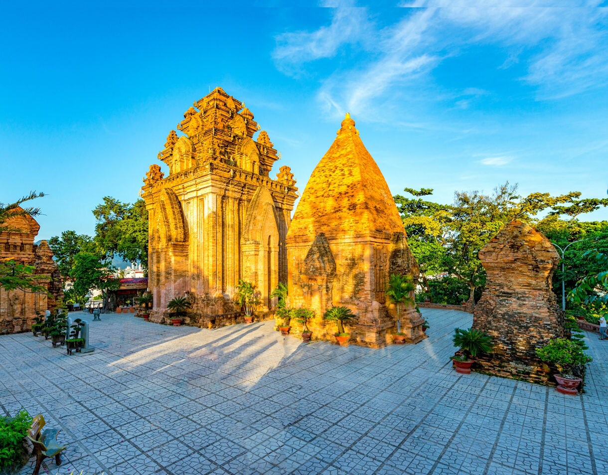 Brick Cham towers at Po Nagar in Nha Trang stand under a bright blue sky with warm sunlight highlighting their detailed carvings.