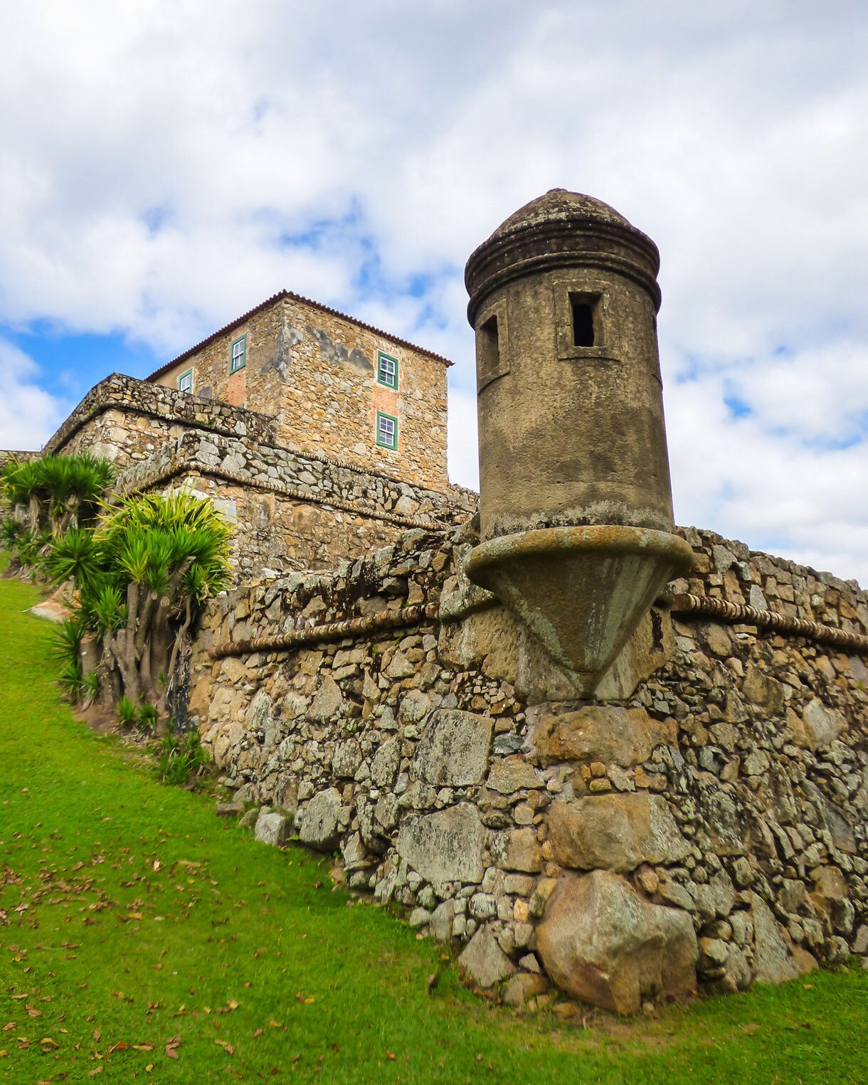 Close-up of a small arched doorway sealed with a rusted iron grid in a worn stone wall, with grass growing at its base.