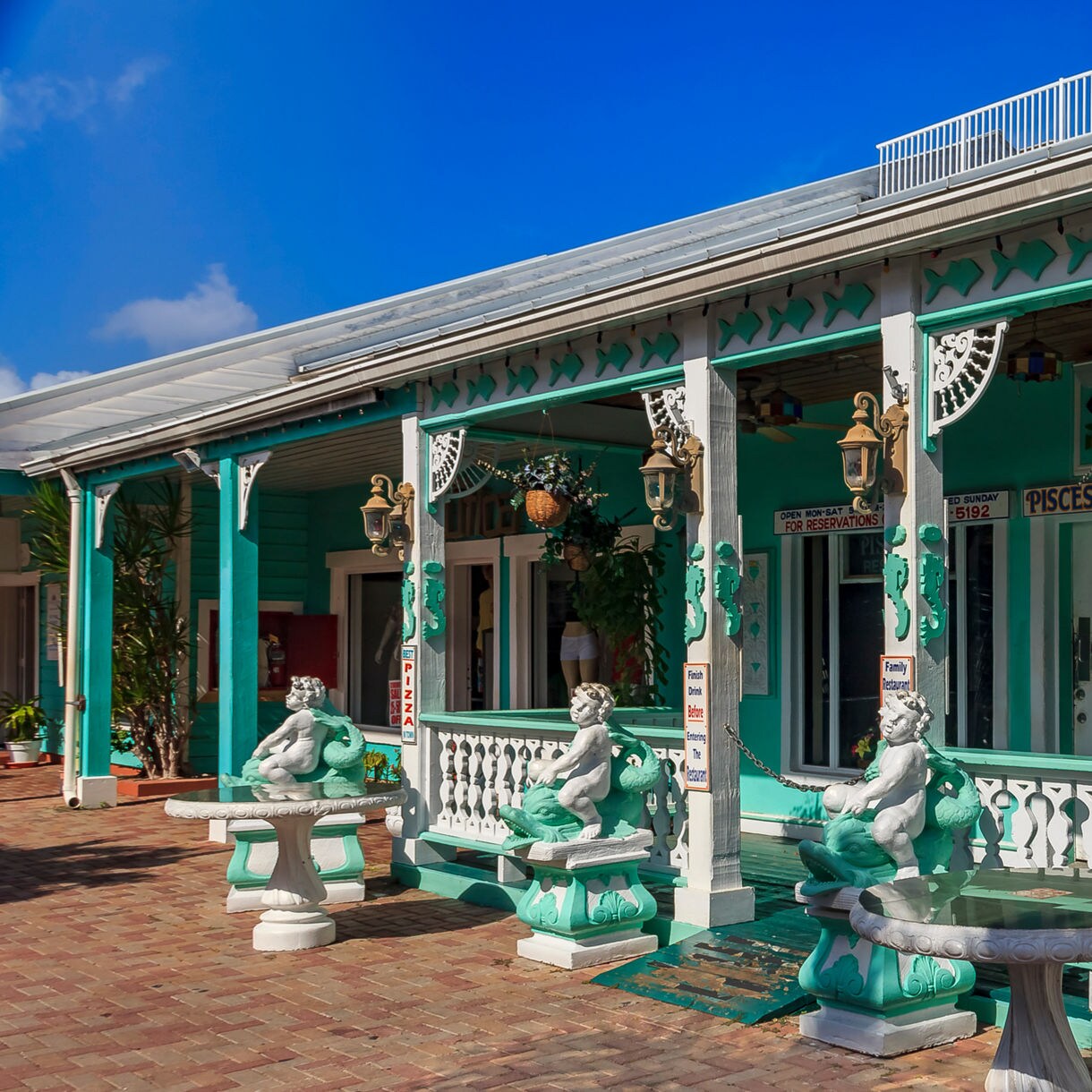 Colorful turquoise building at Port Lucaya Marketplace in Freeport, Bahamas, featuring decorative columns, hanging plants and outdoor seating.