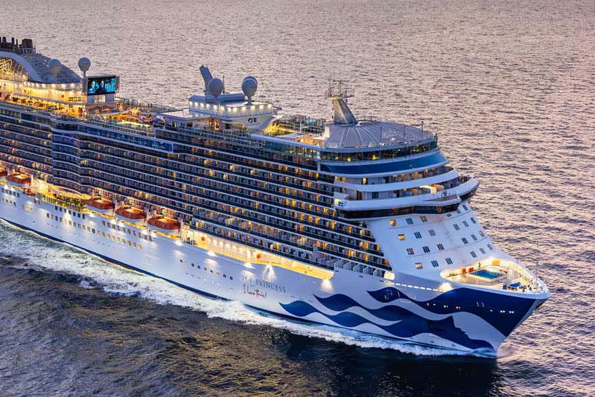 Large Princess cruise ship sailing on open ocean waters with multiple decks visible and the distinctive blue wave logo on its white hull.