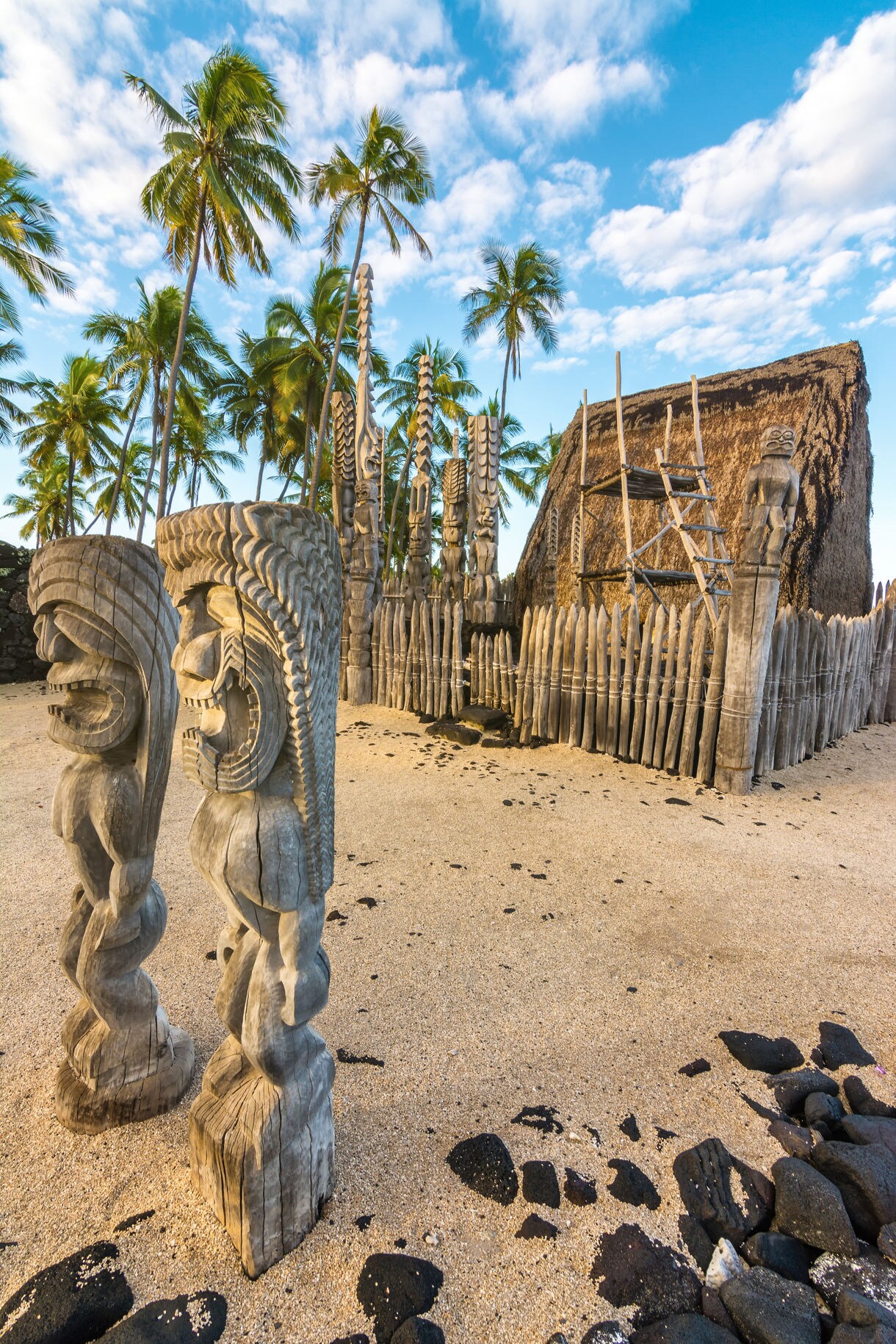 Wooden ki‘i statues and a thatched temple surrounded by palm trees at Puʻuhonua o Hōnaunau National Historical Park on the Big Island.
