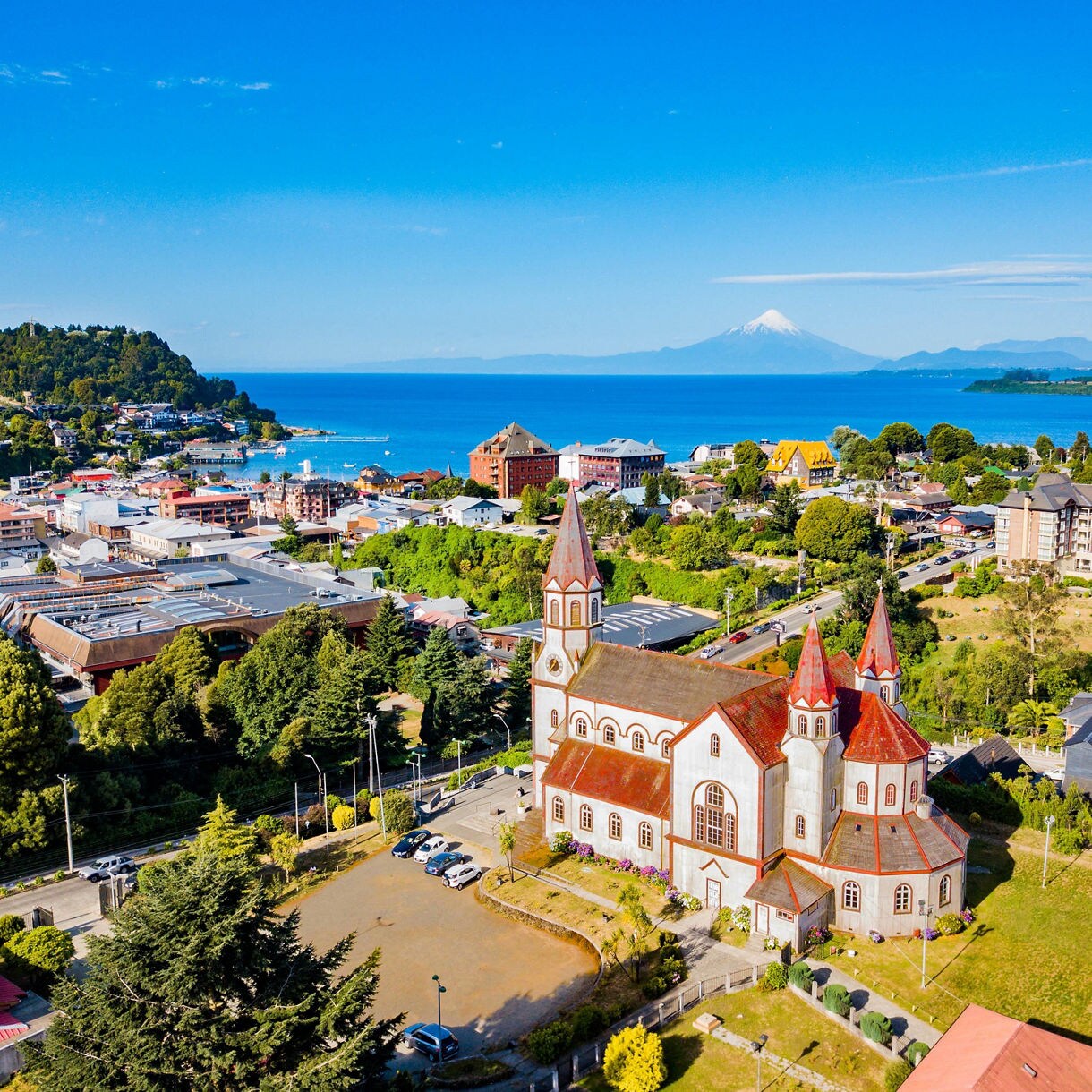 Aerial view of Puerto Varas with its red-roofed church, colorful town buildings and Osorno Volcano towering above Lake Llanquihue.