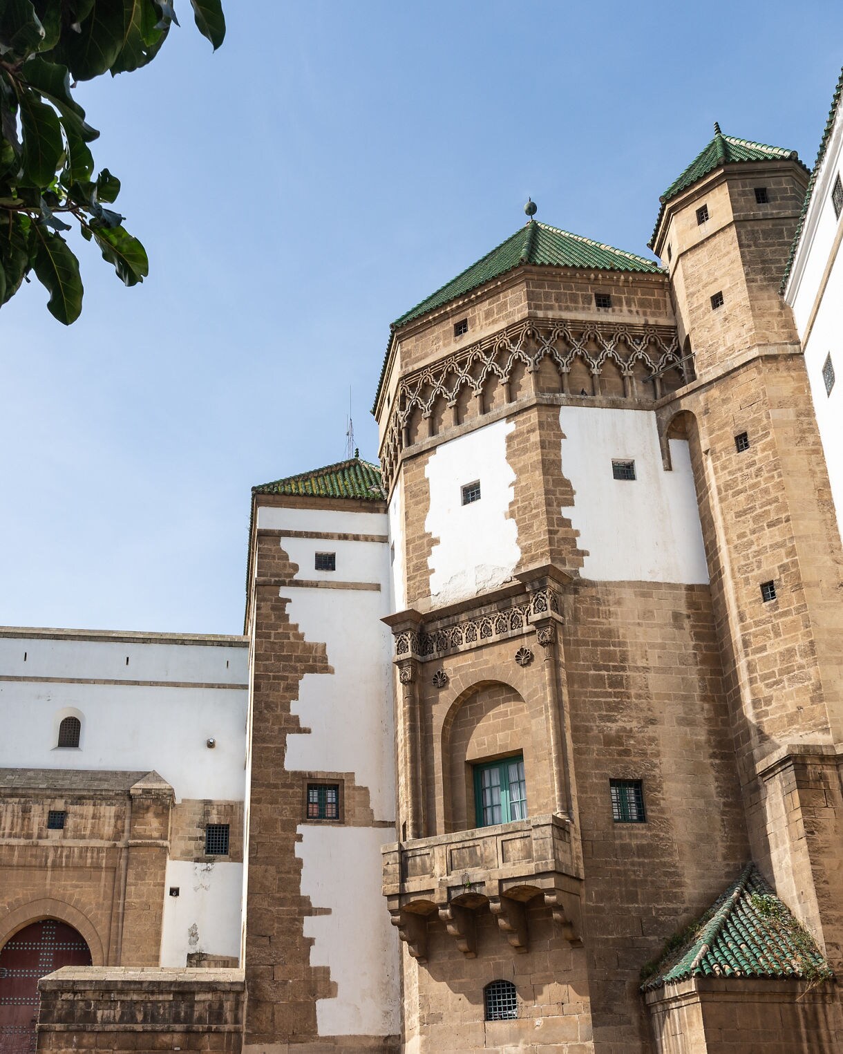Stone and whitewashed buildings with green tiled roofs and arched details under a clear sky.