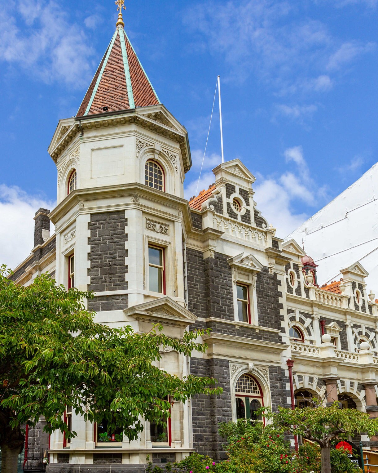Close-up of Dunedin Railway Station’s ornate stone façade and tower under a bright blue sky.