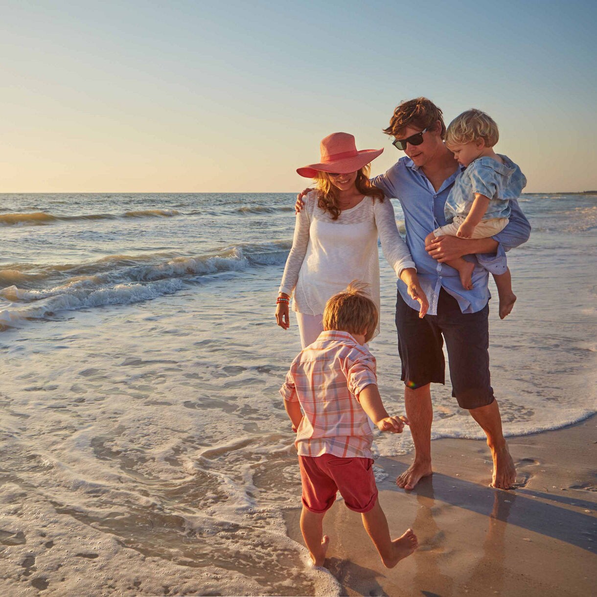Family of four walking by the beach at sunset, enjoying the waves – parents with two young children on a evening.