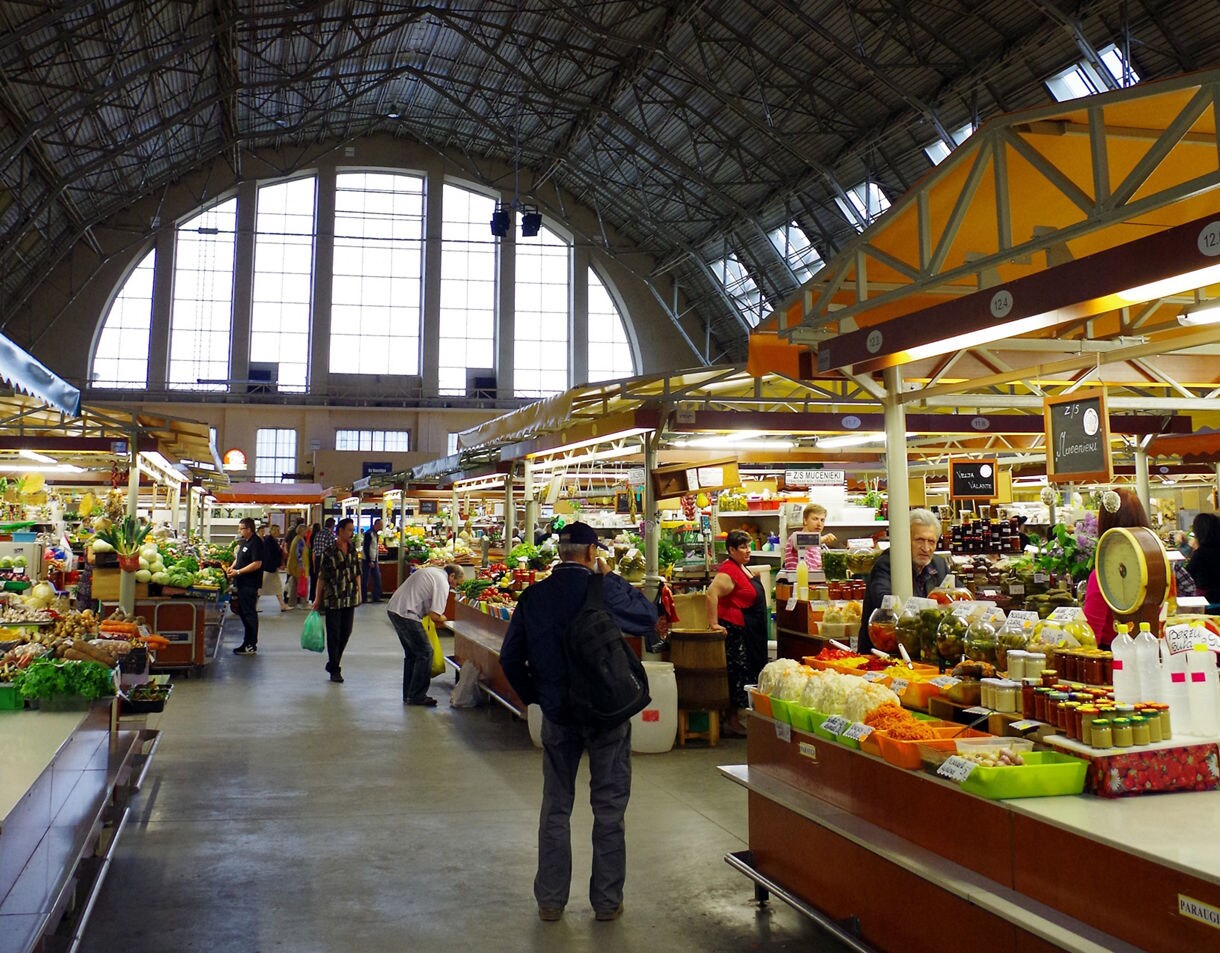 Interior of Riga Central Market in Latvia, showing wide aisles lined with colorful stalls selling fruits, vegetables, preserves and local goods under a towering arched roof.