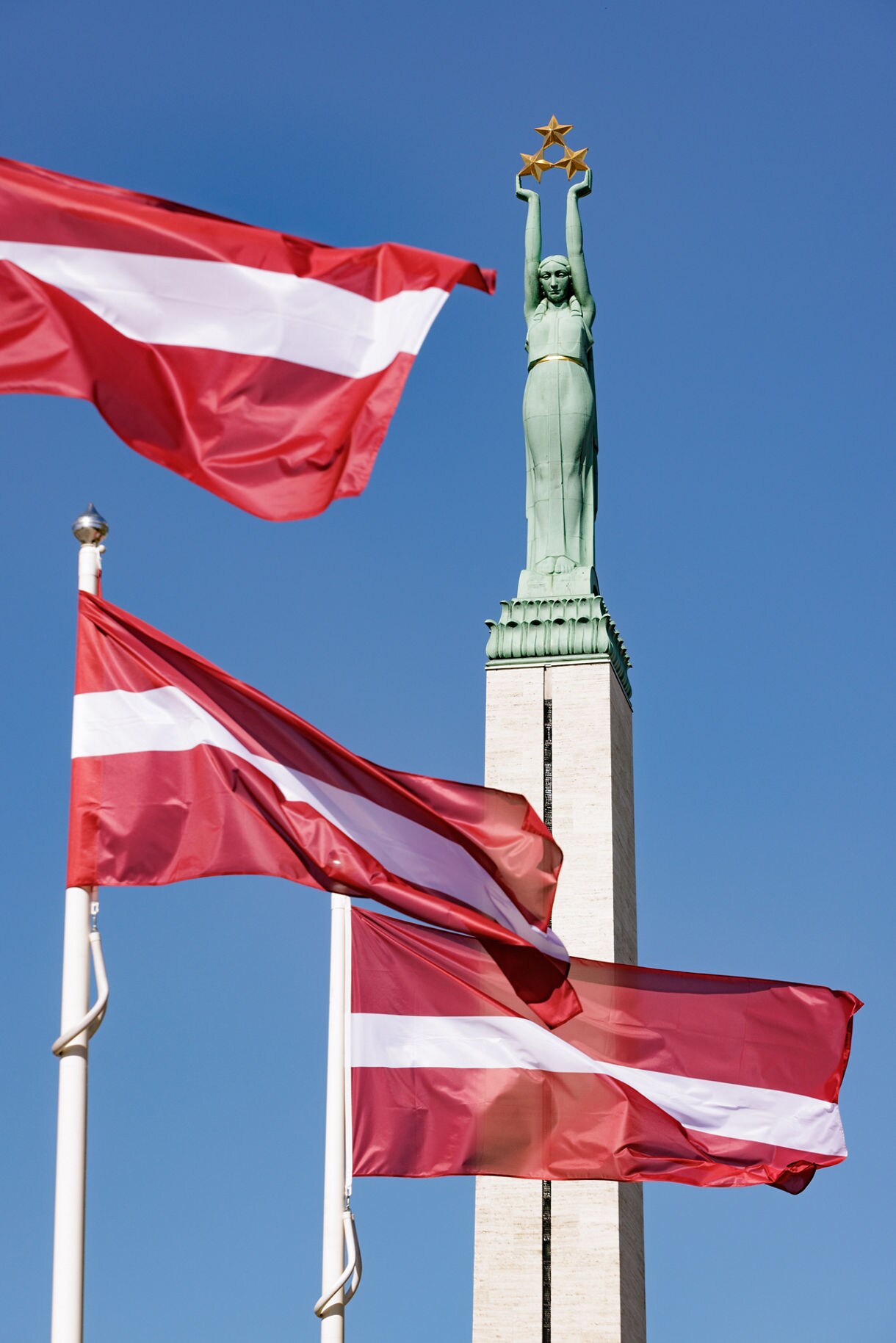Close-up of the Freedom Monument in Riga, Latvia, showing the bronze female figure holding three golden stars aloft against a clear blue sky.