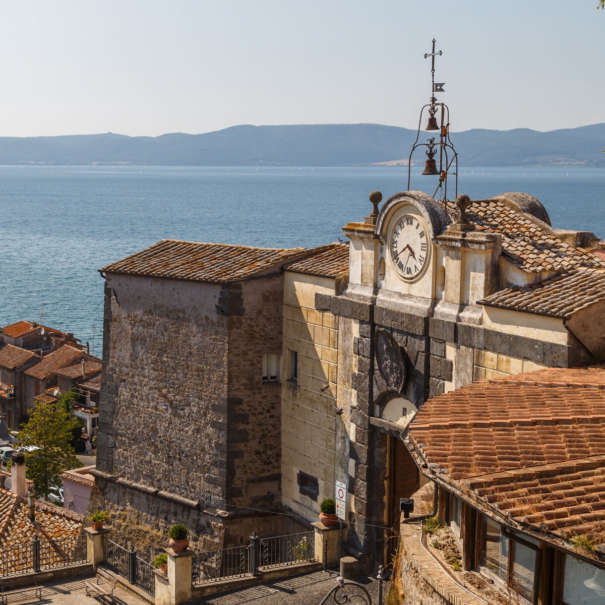 View of Anguillara Sabazia with tiled rooftops, a clock tower, and Lake Bracciano stretching into the distance.