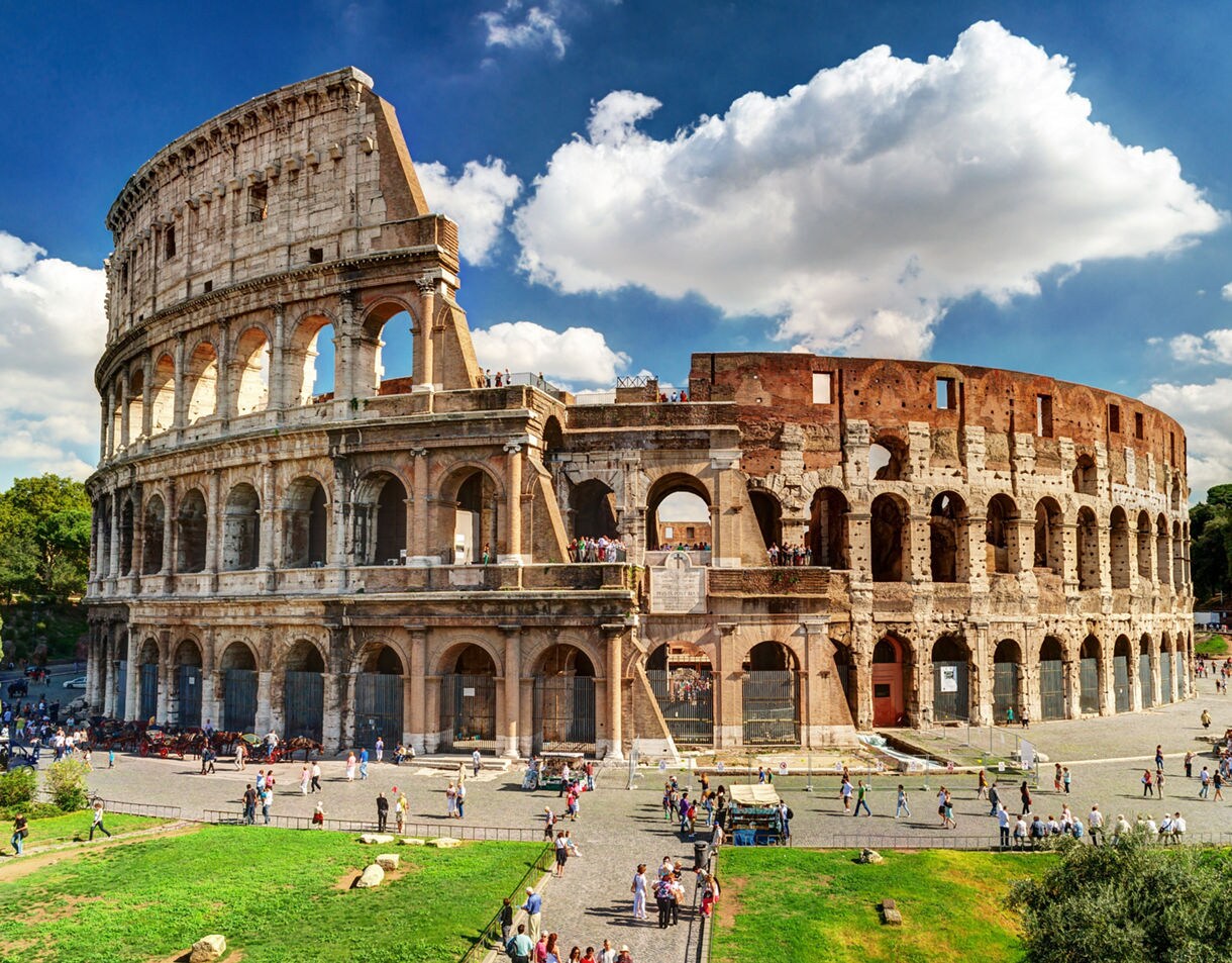 The Colosseum in Rome on a sunny day, with crowds of visitors exploring the iconic oval amphitheater.