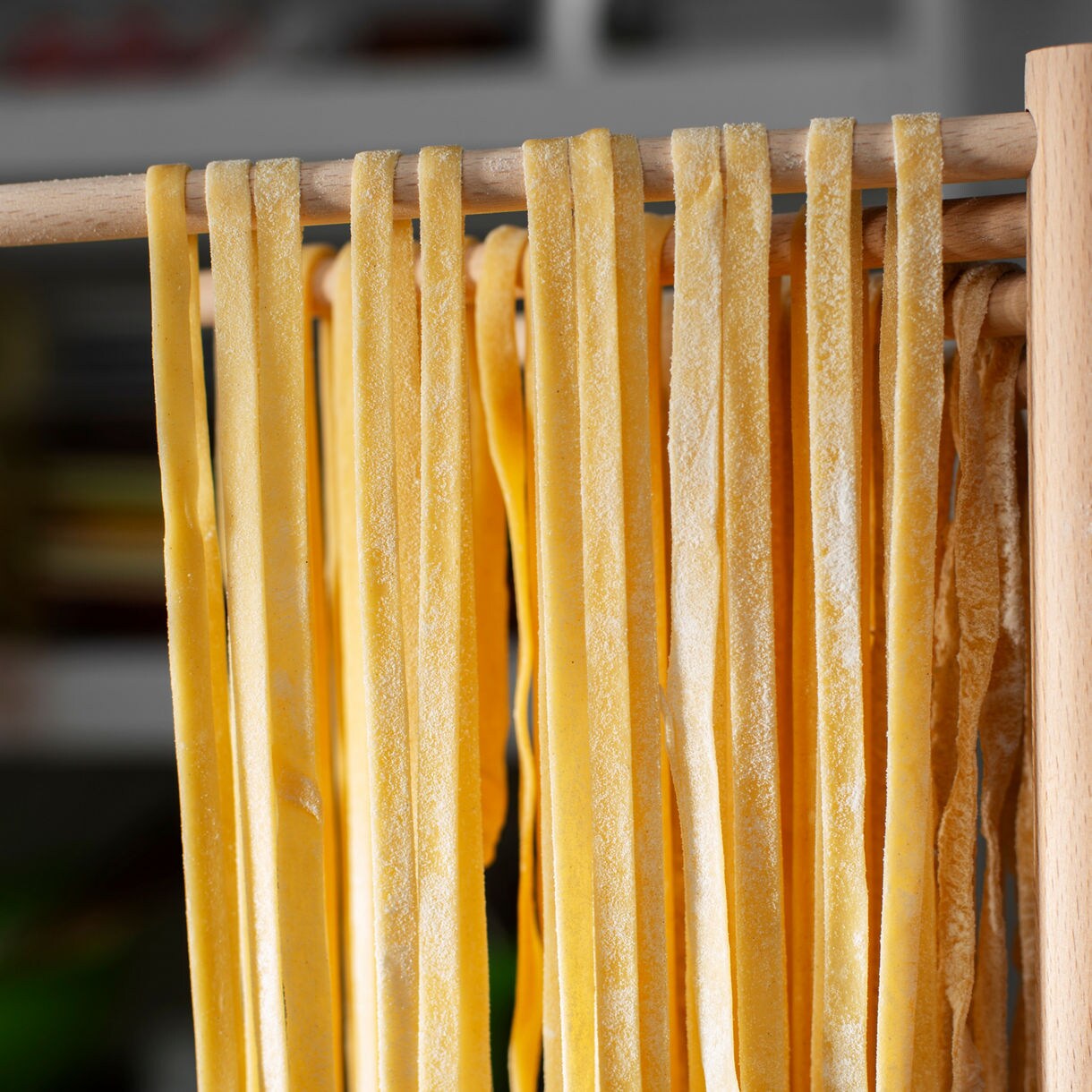 Strands of freshly made pasta hanging on a wooden rack to dry in a kitchen setting.