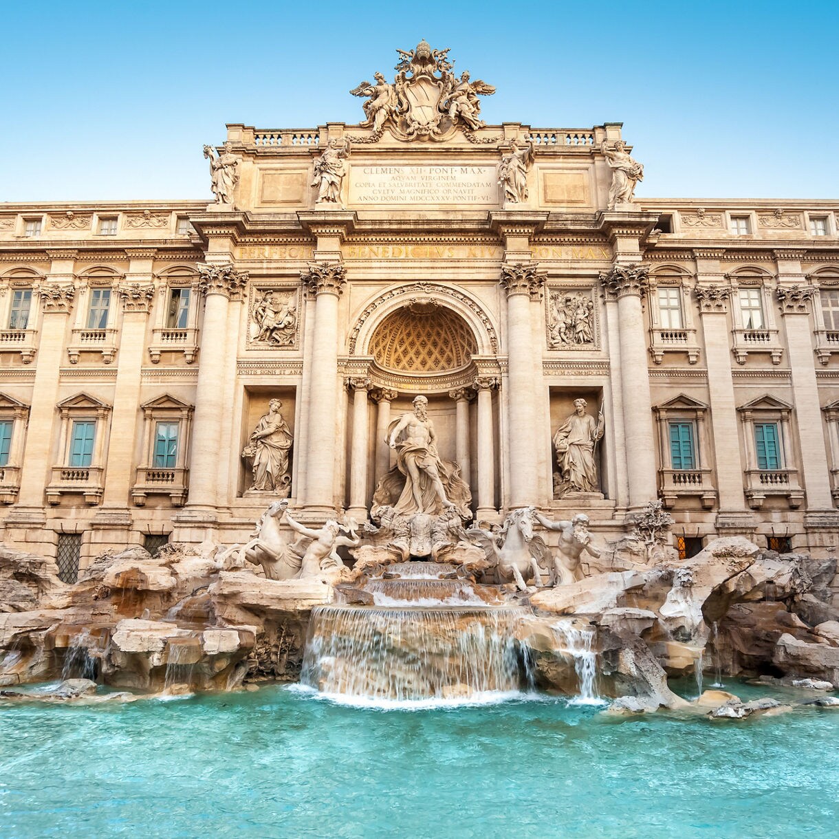 Small neoclassical temple with columns reflected in a tranquil pond surrounded by trees.