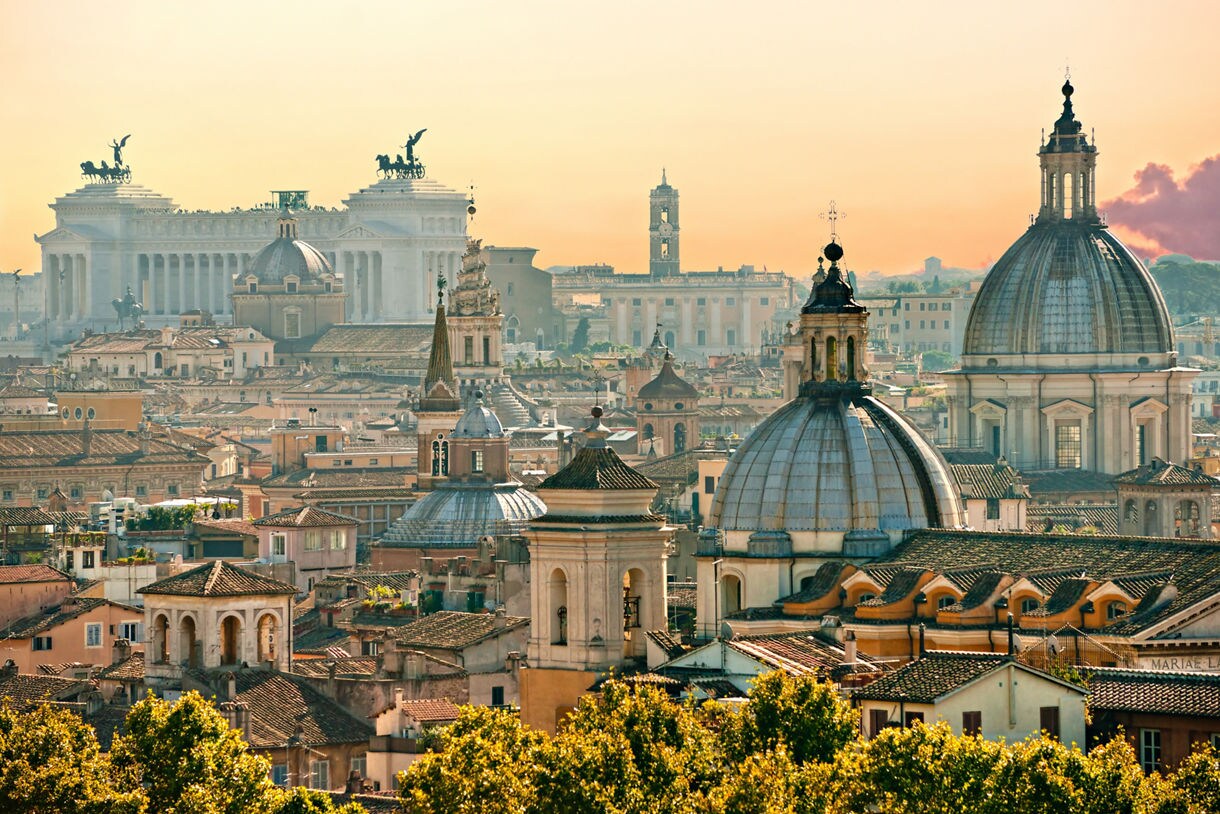 Panoramic view of Rome featuring domed churches, historic rooftops, and the white marble Altare della Patria in the distance.