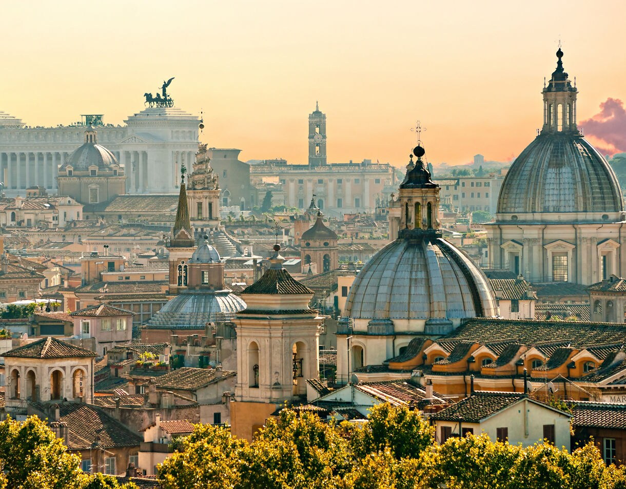 Panoramic view of Rome with tiled rooftops, church domes, and the Altare della Patria in the distance.