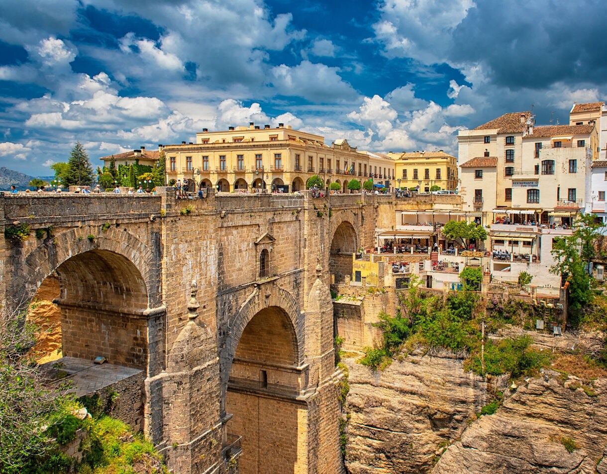 Stone arch bridge Puente Nuevo in Ronda, Spain, spanning a deep gorge with historic buildings perched along the cliff edge.