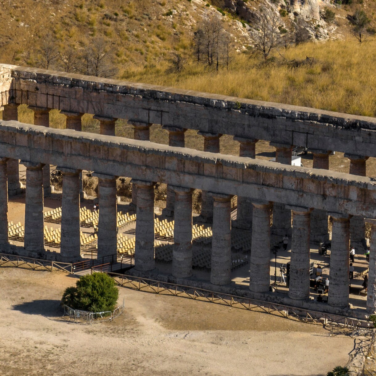 A well-preserved ancient Greek temple at Segesta in Sicily, with tall stone columns and no roof, set on a dry grassy hillside.